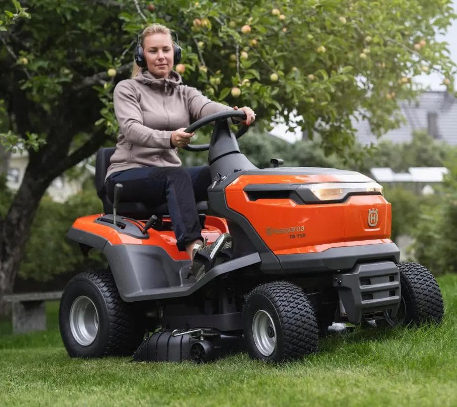 woman sitting on a husqvarna rider underneath lemon tree with protective earmuffs on